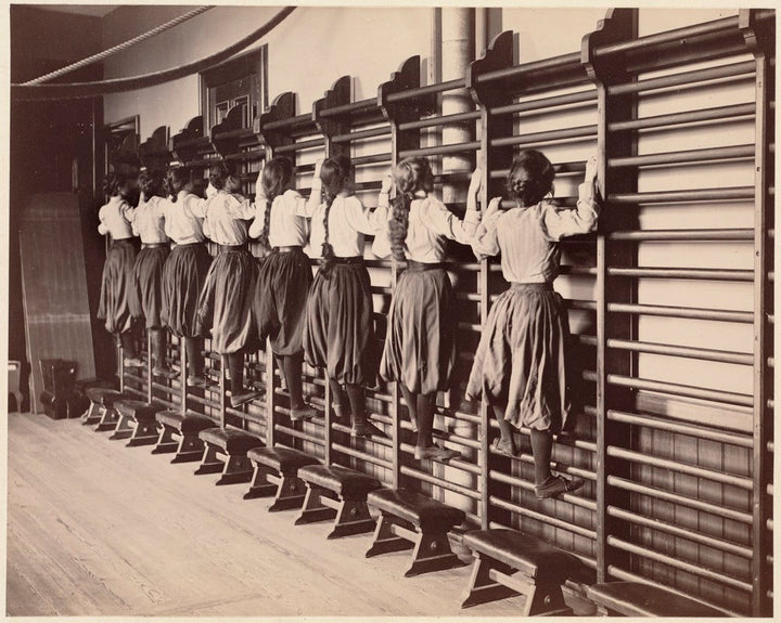 Girls exercising on bars against the swedish ladder wall bars, Charlestown High School, Massachusetts, 1899